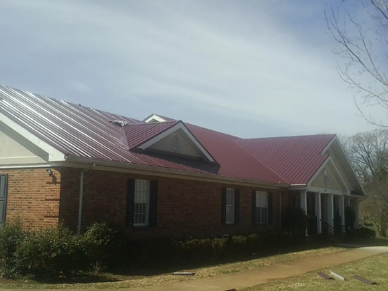 Red metal roof with gabled entries on a long brick building, from a Hail Damage Roof Repair job in Kyburz