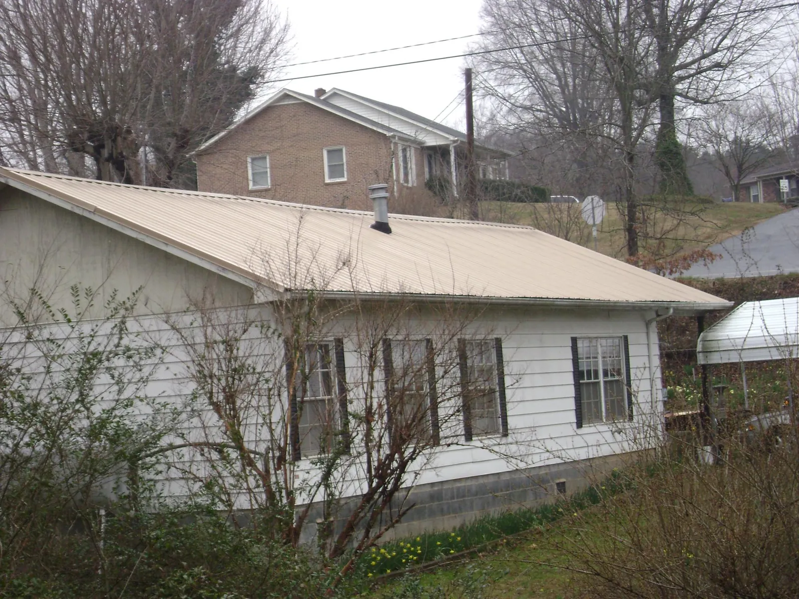 Tan metal roof on a white sided house set into a hillside — Commercial Roofing by Roofing Brothers in Kyburz